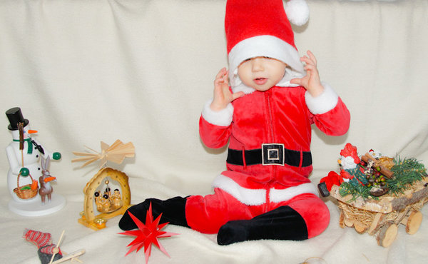Kind im Weihnachtsmannkostüm sitzt in Weihnachtsdeko